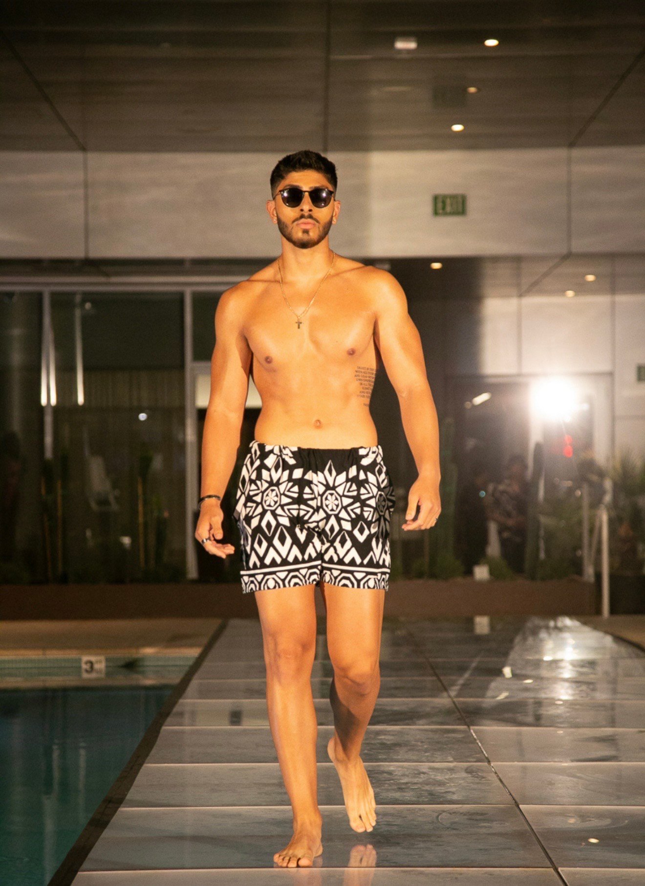 Male model wearing patterned swim trunks by Jaq Lawrence, showcasing modern luxury swimwear and resort-style mens fashion